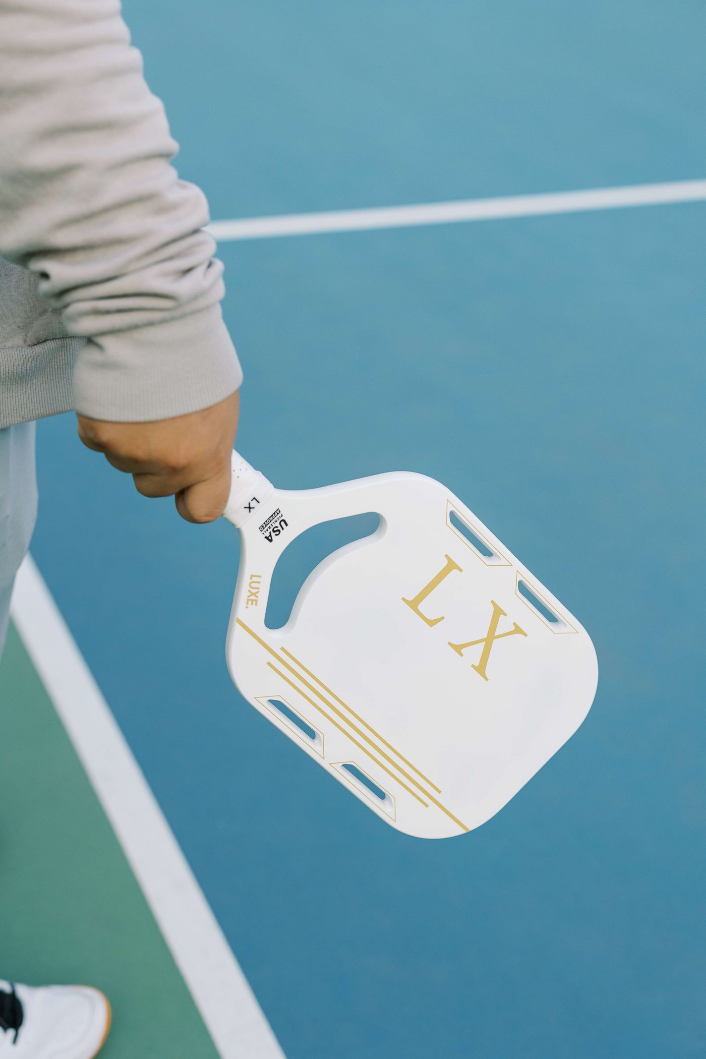 Hand holding a pickleball paddle over a blue outdoor court